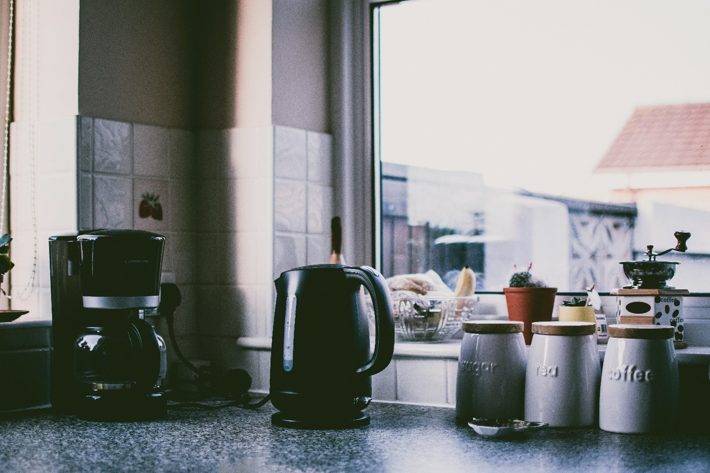 A quartz kitchen top with a coffee pot, electric kettle, and some jars.