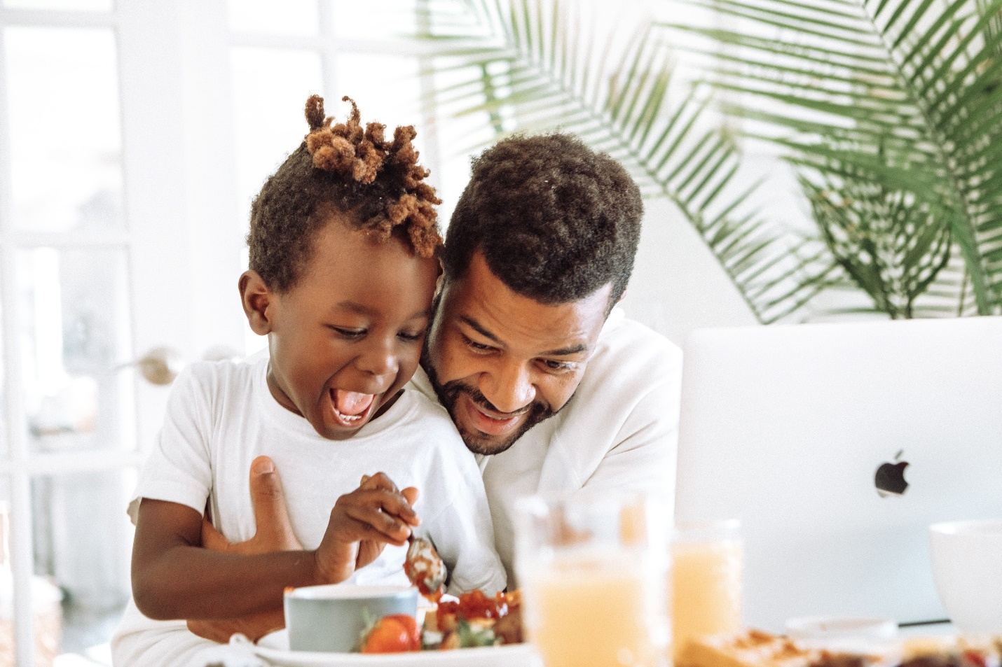 A man interacts playfully with his child during mealtime in the kitchen