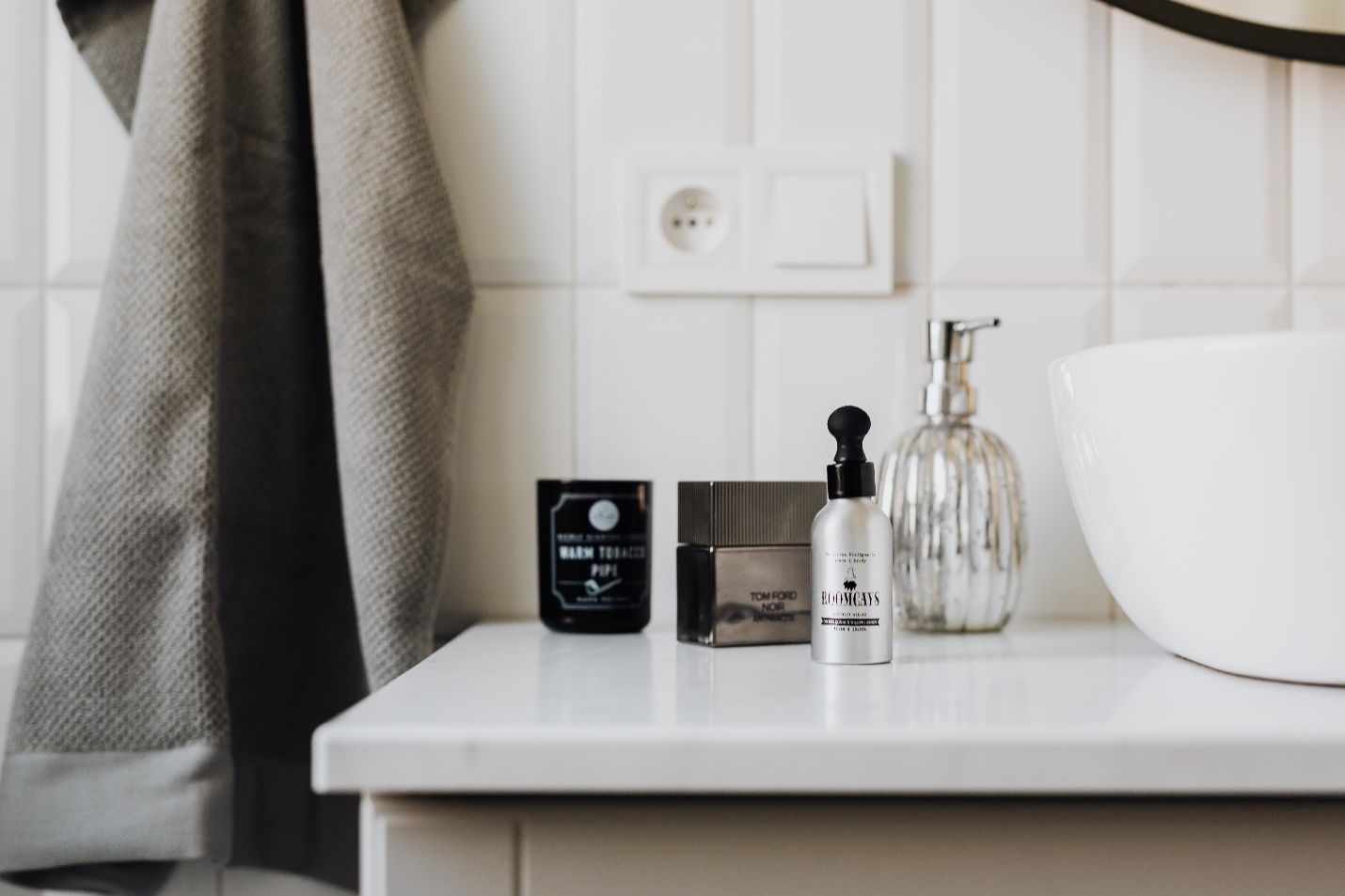 Toiletries sit on a white bathroom vanity top beside a grey face towel