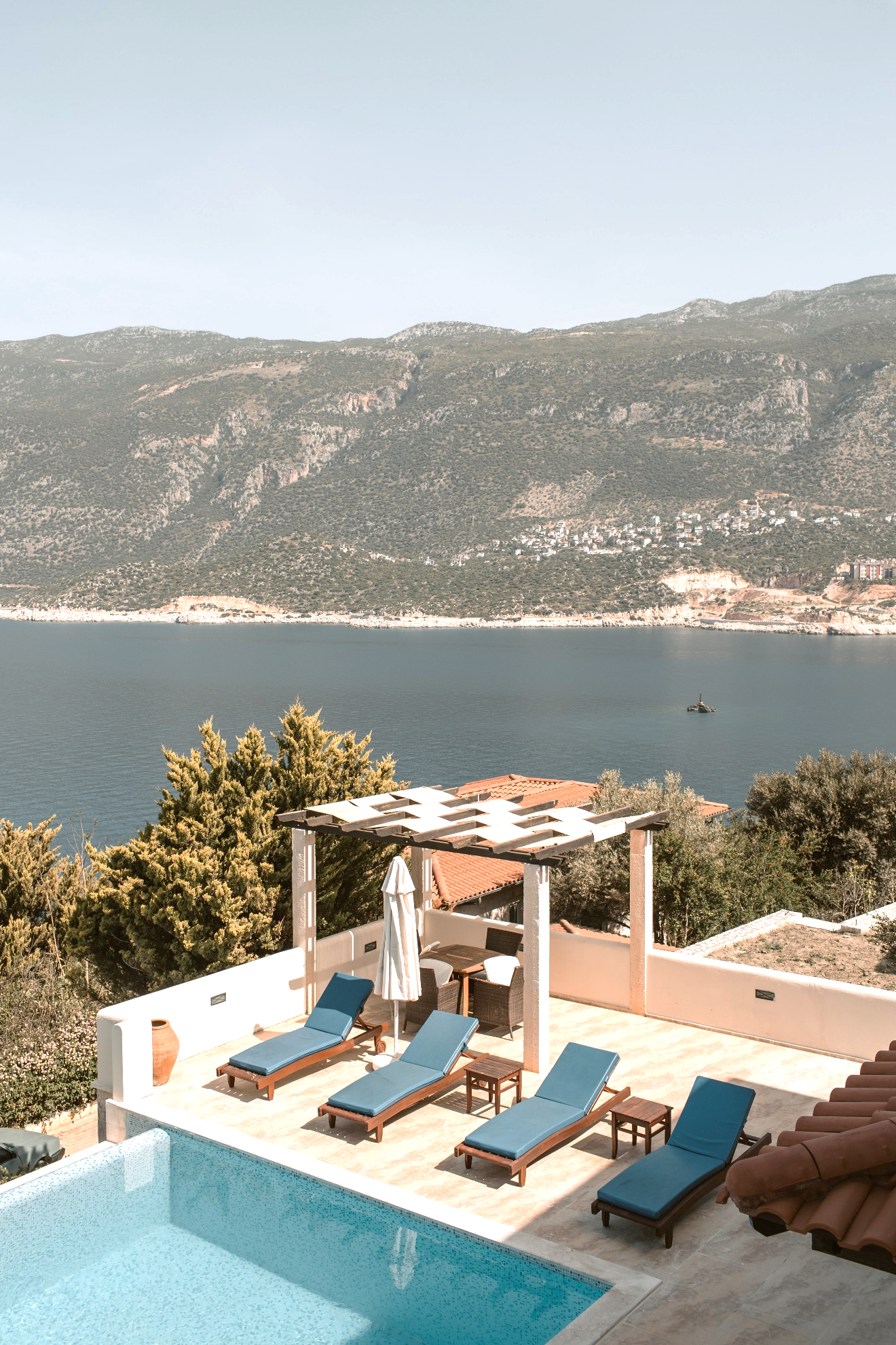 An outdoor pool with deck chairs against the backdrop of a sea